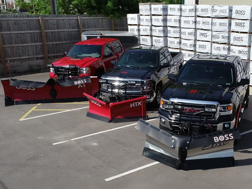 BOSS Plow Lineup — Mid-State Truck Equipment Fishers Greenfield IN BOSS XT, HTX, and poly snow plows on trucks at Mid-State Truck Equipment's lot, with stacked BOSS product inventory behind them